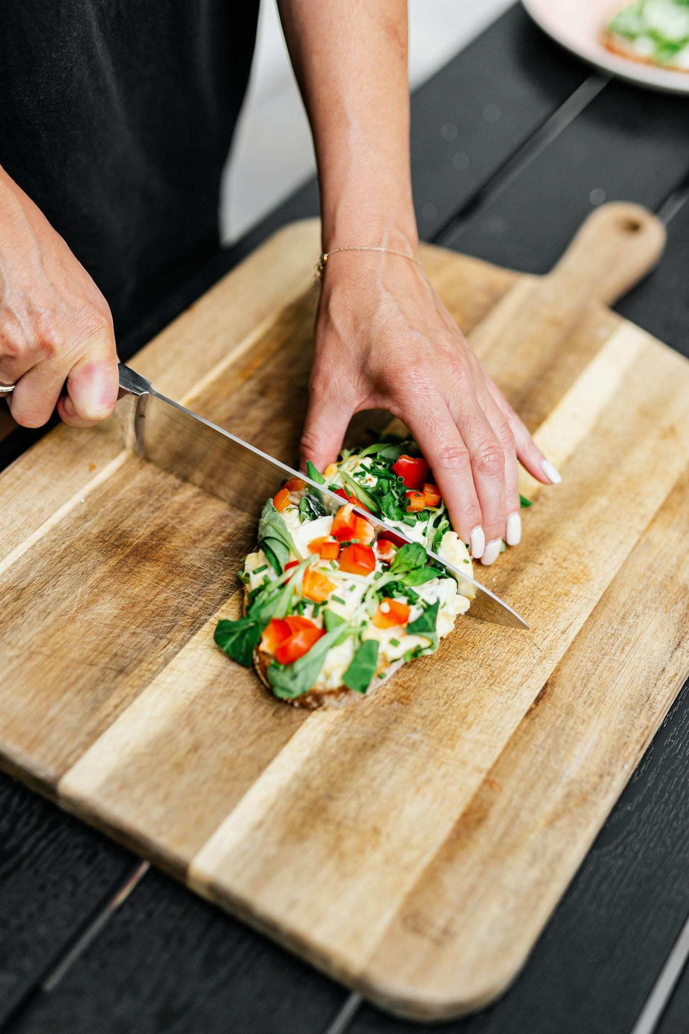 A person cuts a healthy avocado toast topped with vegetables on a wooden board. Ideal for culinary and lifestyle themes.