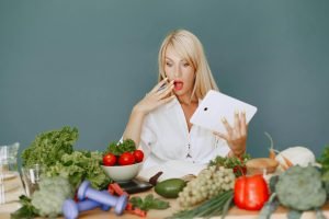 A surprised woman looking at a tablet surrounded by fresh vegetables and fruits, promoting healthy eating.