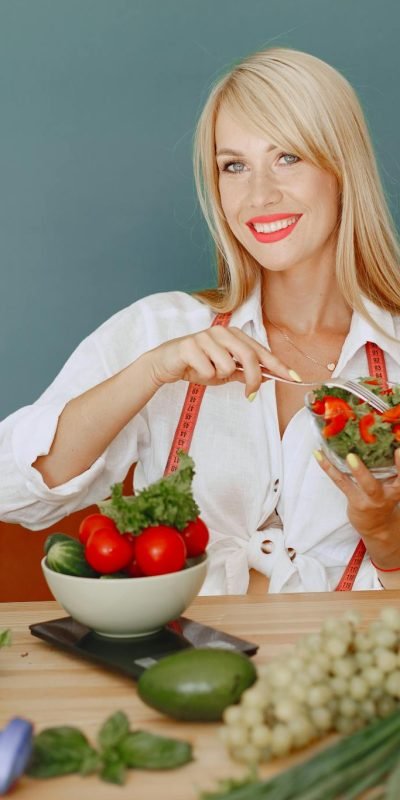 Blonde woman enjoying a fresh salad surrounded by vegetables, promoting healthy eating.