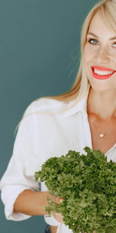 Cheerful woman with blonde hair holding fresh lettuce, promoting healthy living in a studio setting.