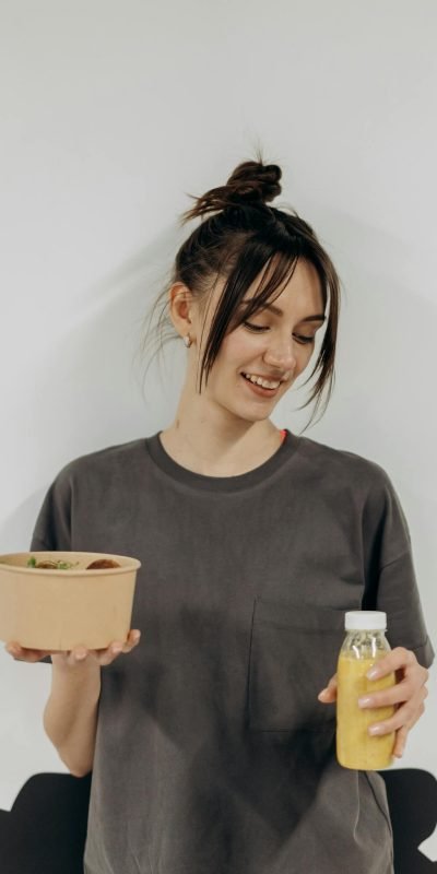 Photo by Mikhail Nilov Woman holding a healthy meal bowl and juice, promoting nutritious lifestyle indoors.