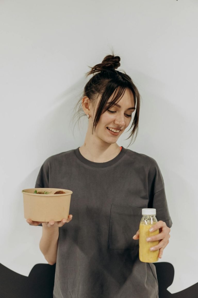 Woman holding a healthy meal bowl and juice, promoting nutritious lifestyle indoors.