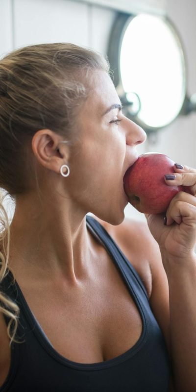 Young woman in a tank top eating an apple for a healthy snack indoors.