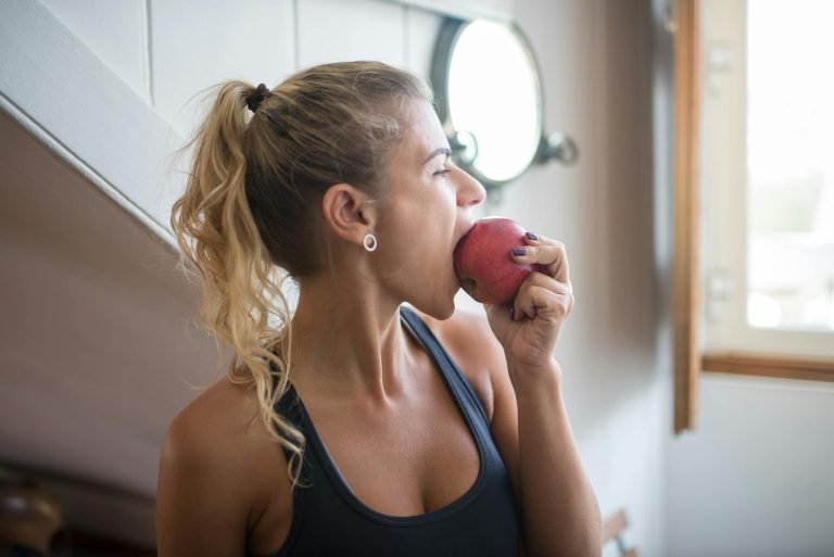 Young woman in a tank top eating an apple for a healthy snack indoors.